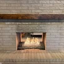 Brick fireplace with lit decorative faux logs and a wooden mantel.