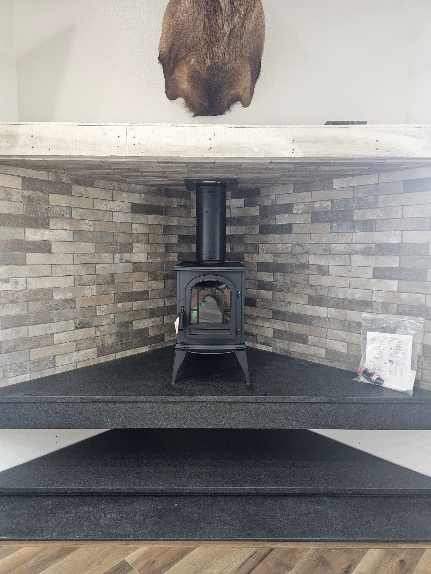 Black stove centered in a brick fireplace, beneath a gray mantle. A fur rug hangs above.