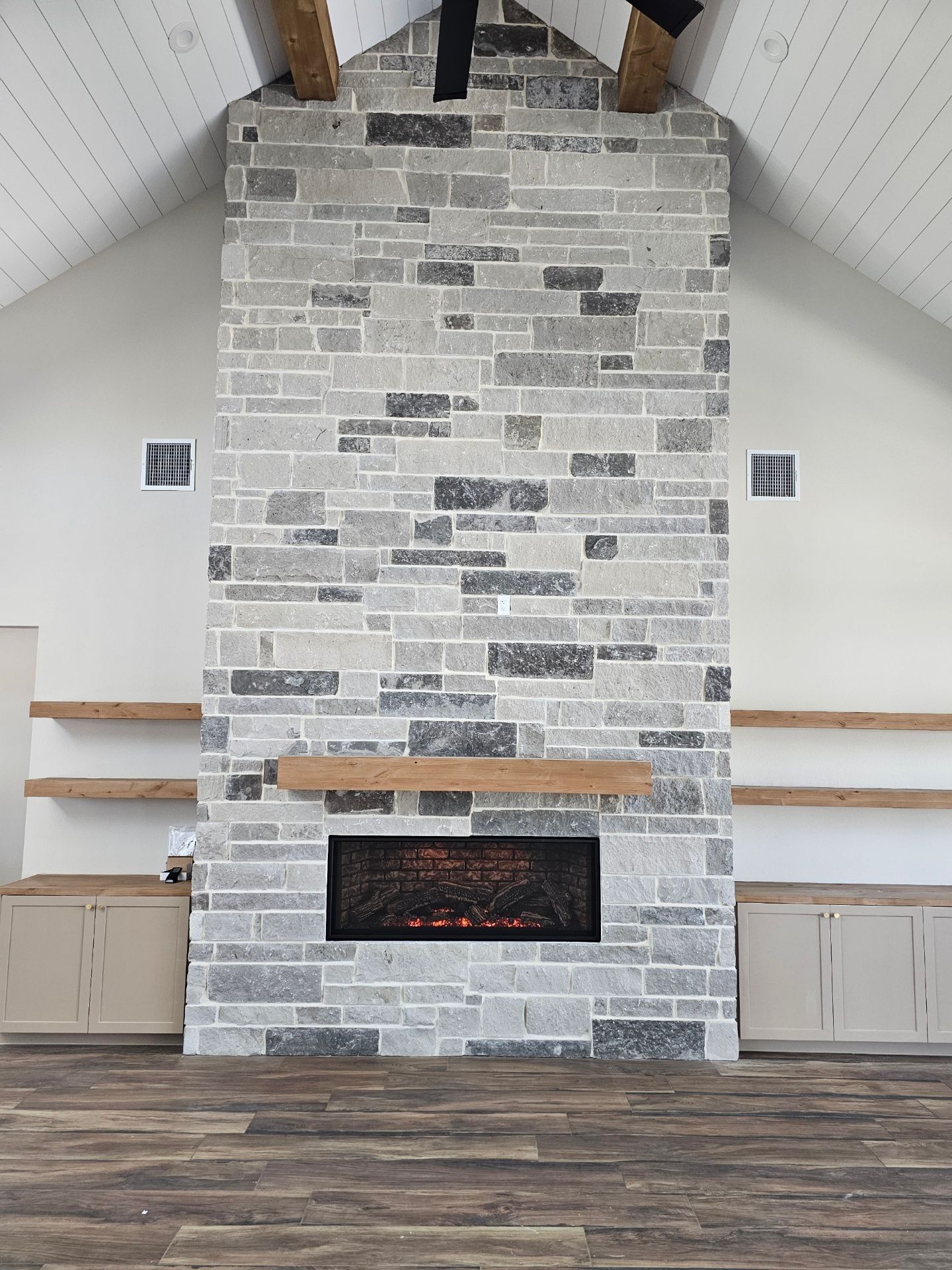 Stone fireplace with a wooden mantle and shelves, set in a room with a high ceiling.