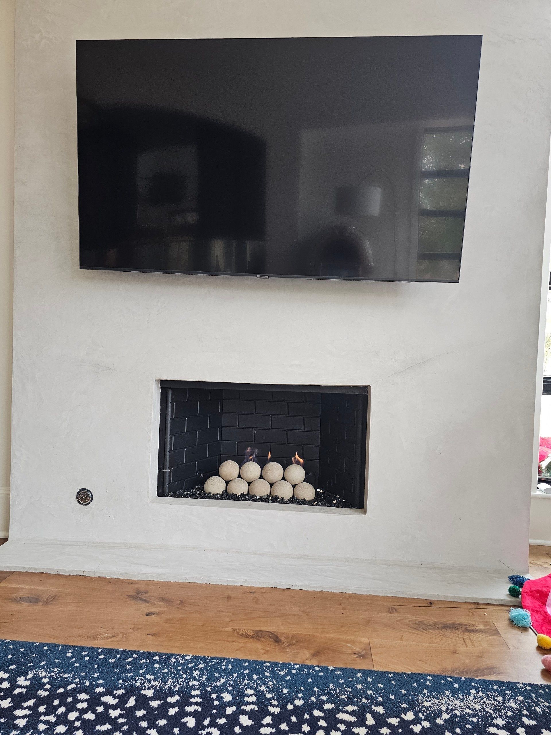 TV above fireplace with glowing decorative balls. White wall and rug in a room.