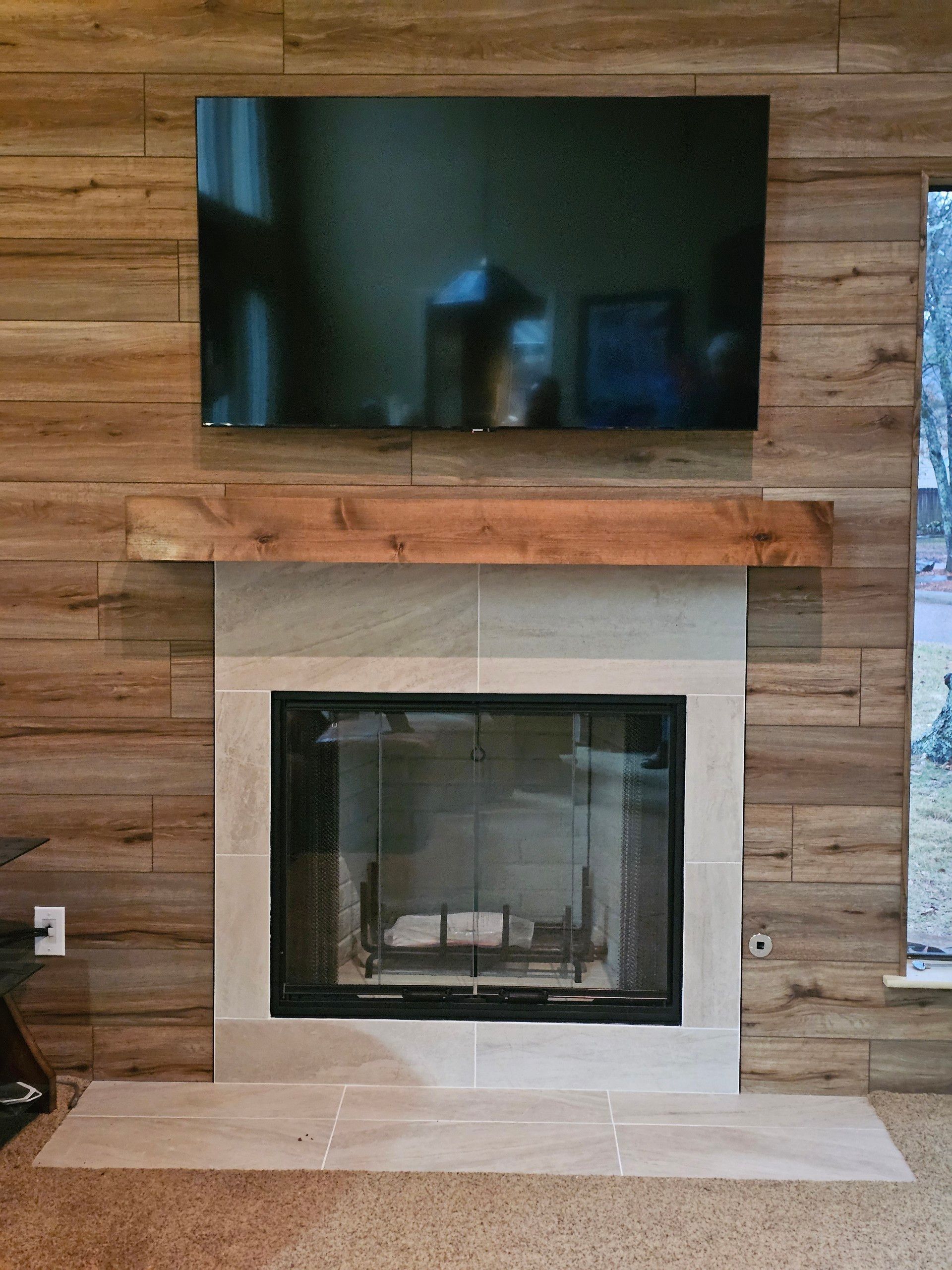 Fireplace with a mounted TV, wood paneling, and a natural stone surround and hearth.
