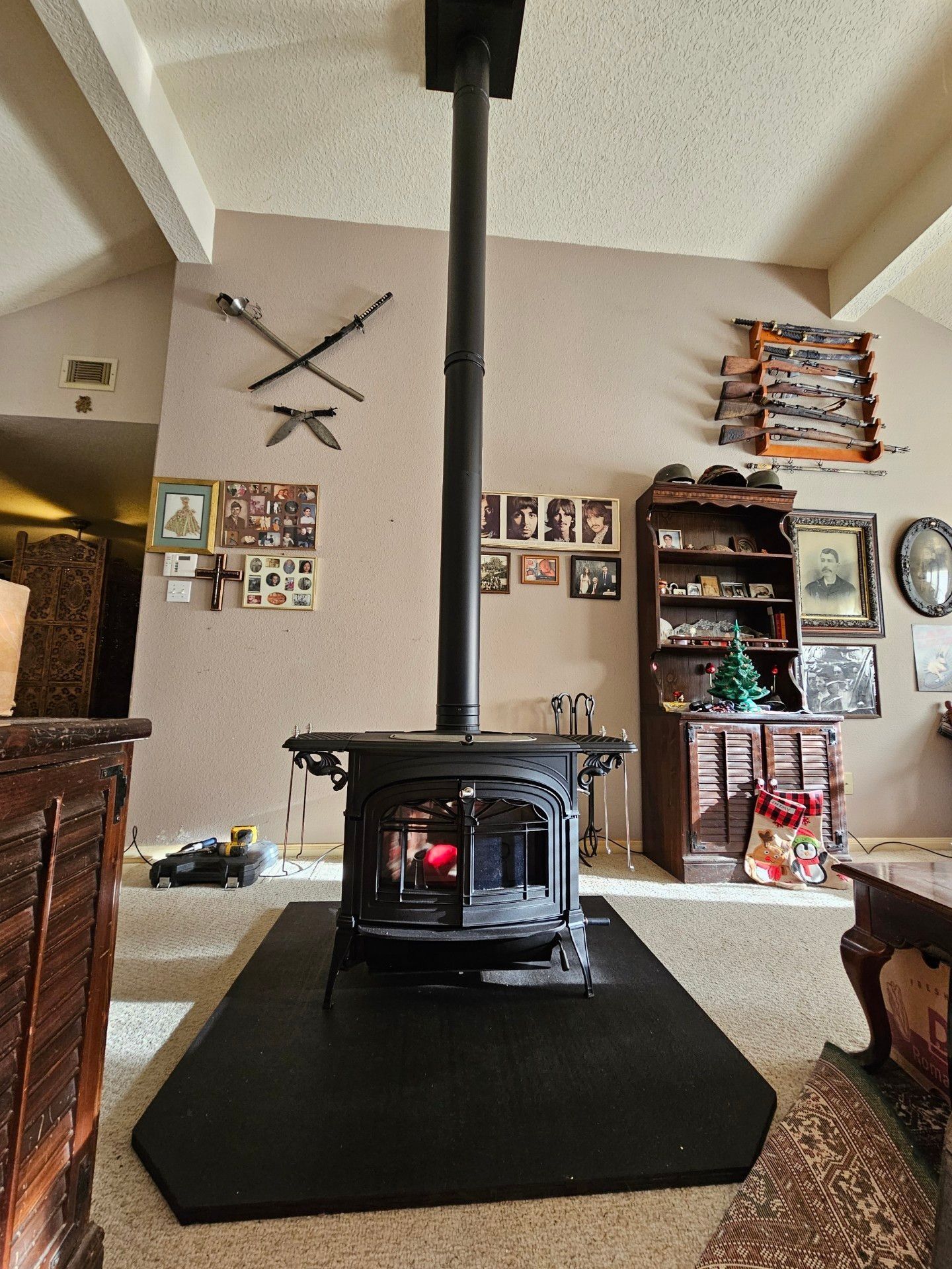 A wood-burning stove with black chimney, centered in room. Decorations and furniture surround it.