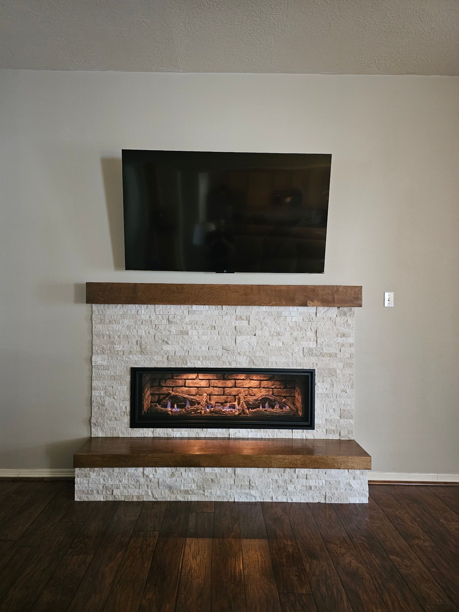 Fireplace with stone facade, dark wood mantel and base, a mounted TV, and a simulated fire effect.