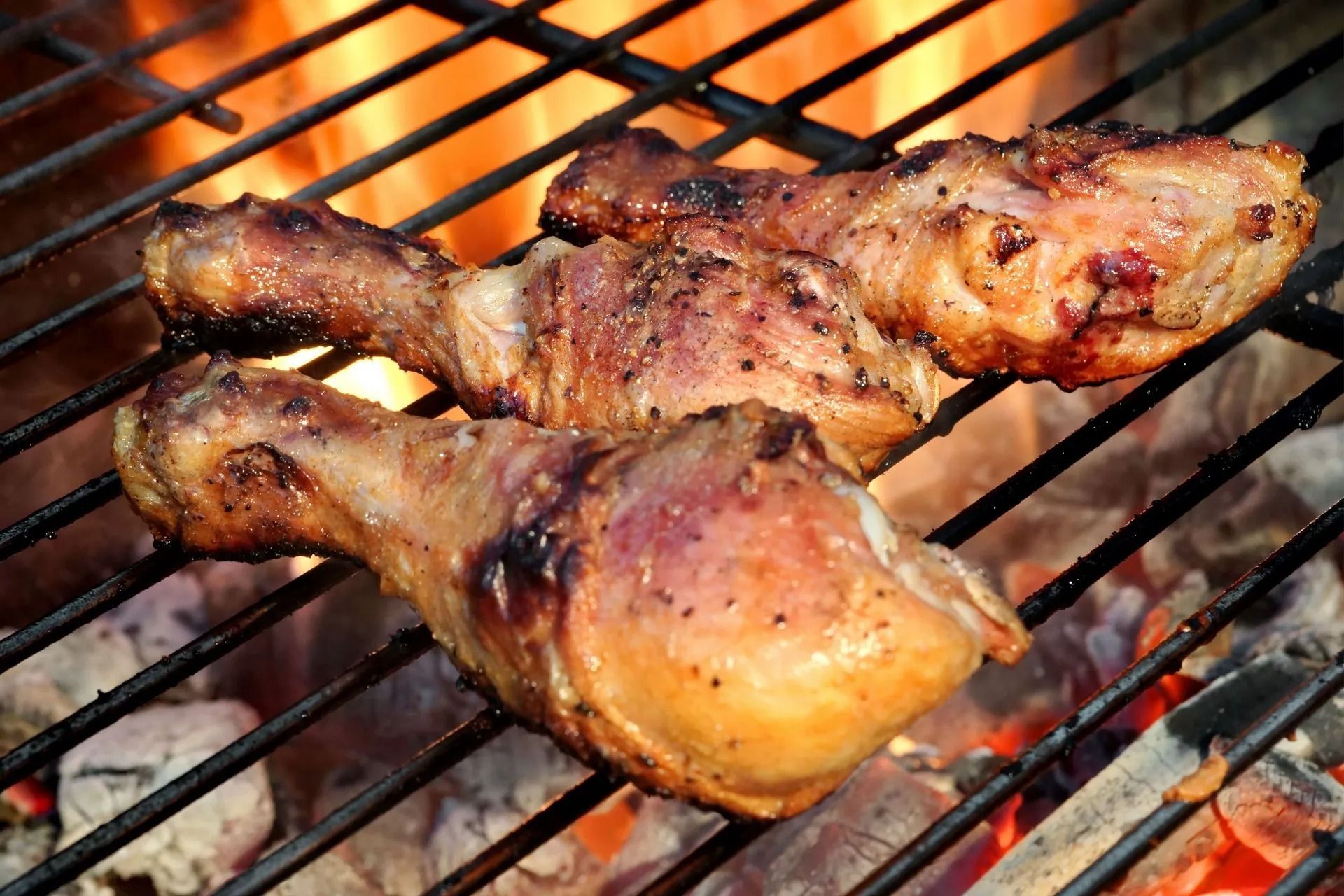 Grilled chicken drumsticks on a hot barbecue grill with flames.