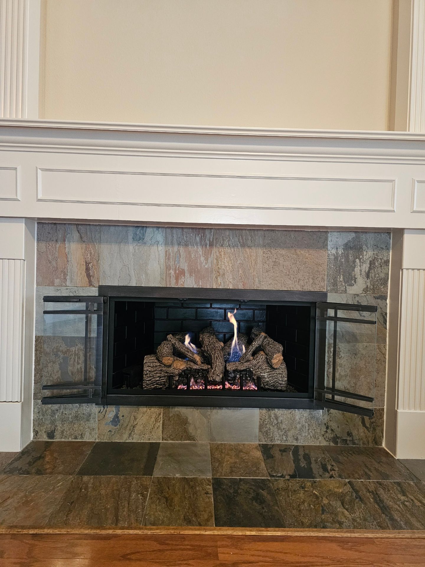 Fireplace with slate tile surround, white mantel, and burning gas logs.