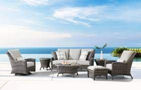 Outdoor wicker furniture set on a patio overlooking the ocean under a blue sky.