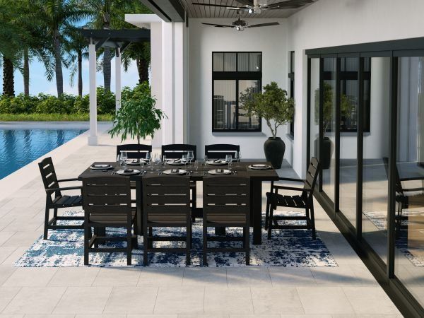 Outdoor dining set on a patio by a pool, dark brown furniture, blue rug, and tropical plants.