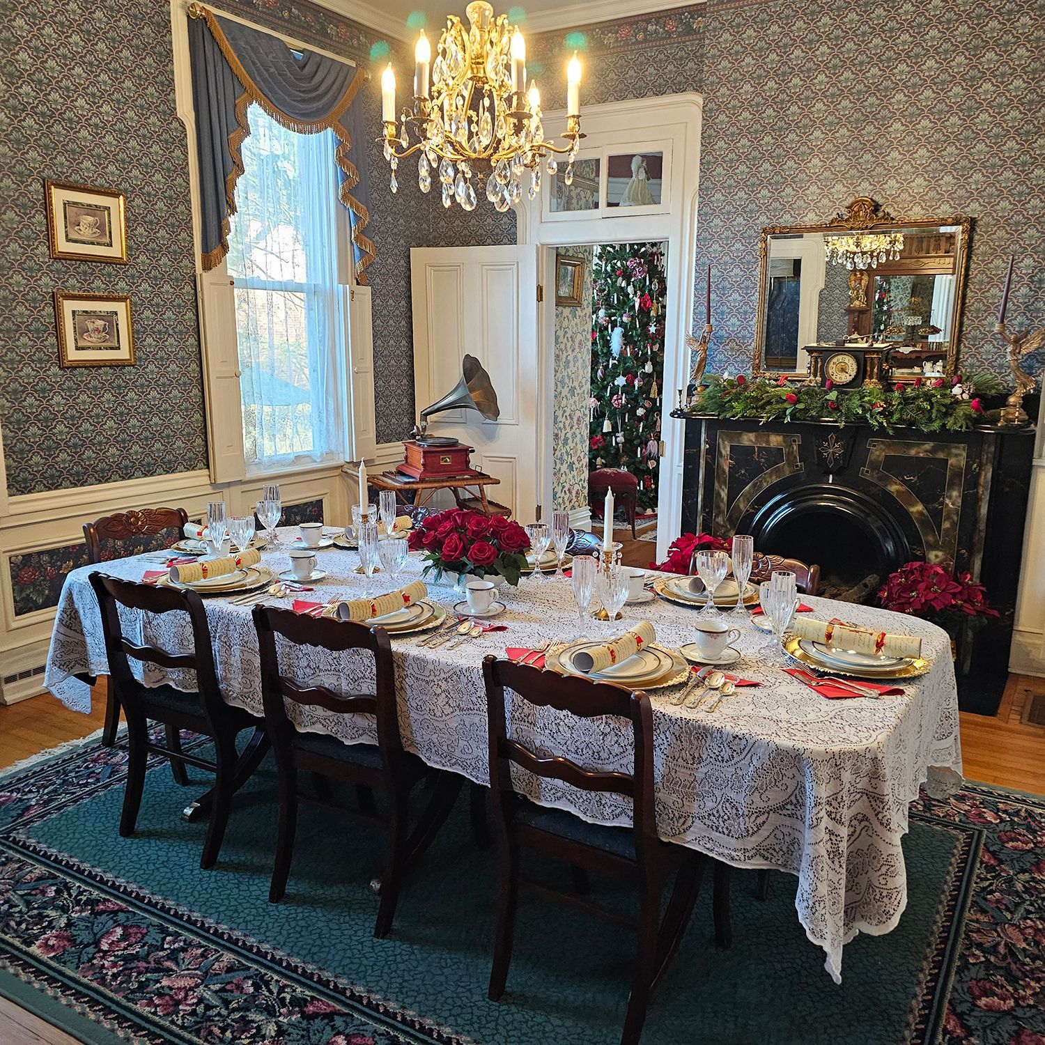 Elegant dining room set for a meal, with a long table, chairs, and fireplace. Festive decorations and floral arrangements enhance the space.