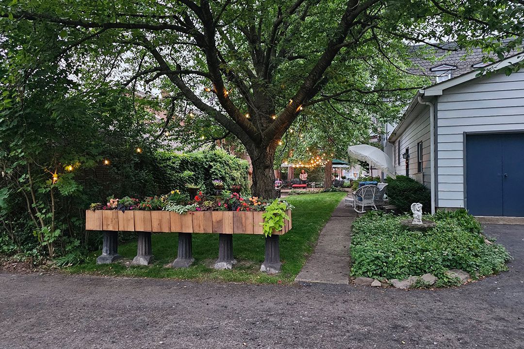 A backyard garden with a large tree strung with lights, a wooden planter, and a garage.