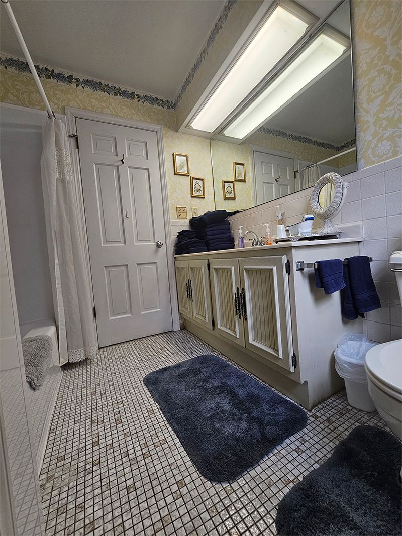 Bathroom with white cabinets, patterned tile floor, and a blue bathmat. White door, and blue towels.