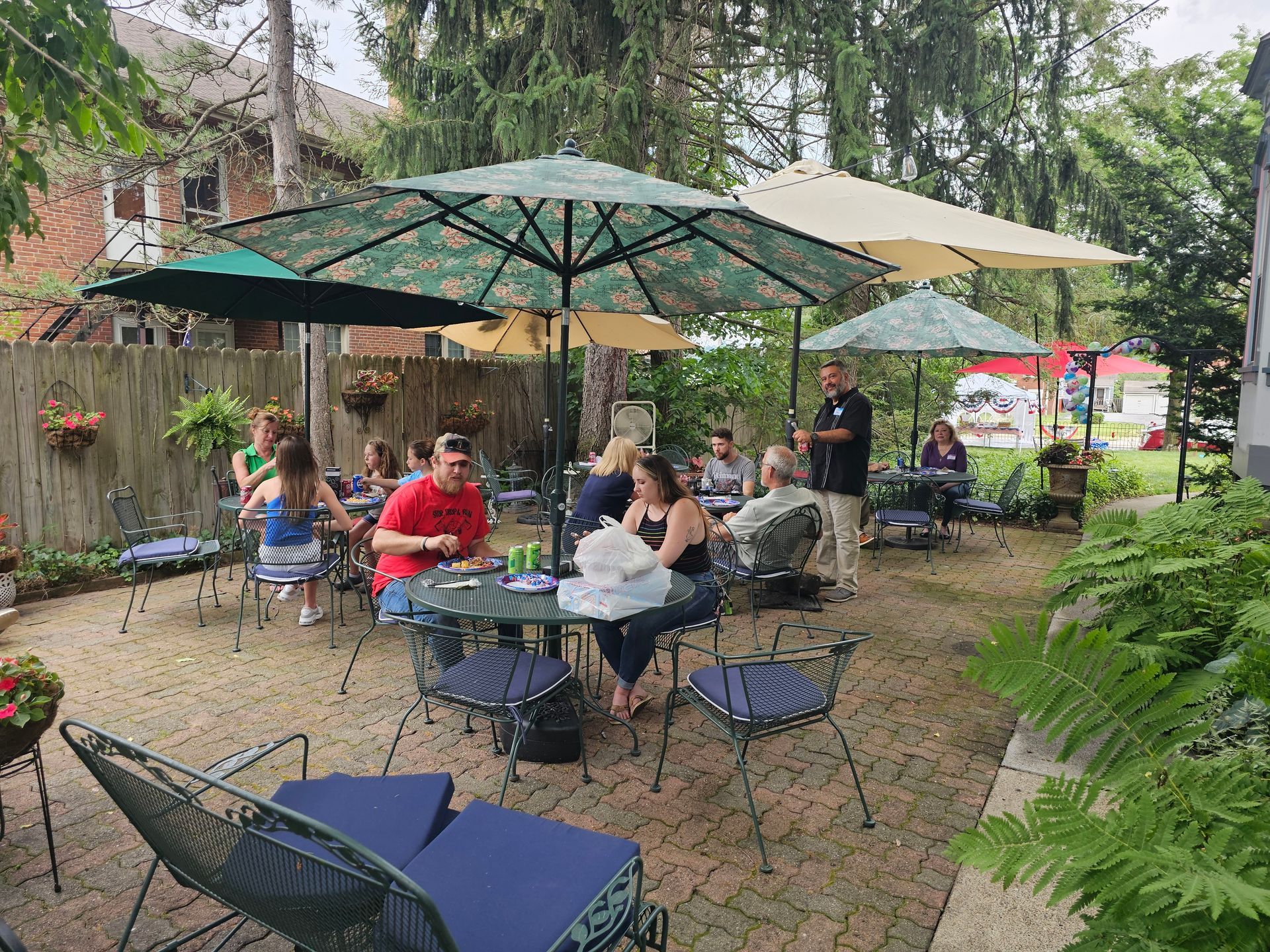 A group of people are sitting at tables under umbrellas in a backyard.