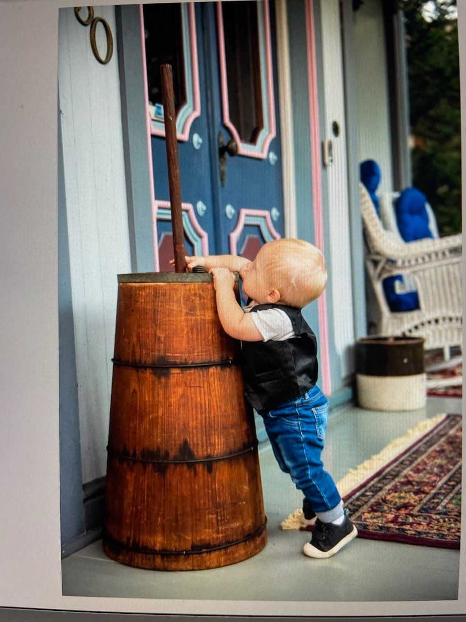 A little boy leaning on a wooden barrel on a porch