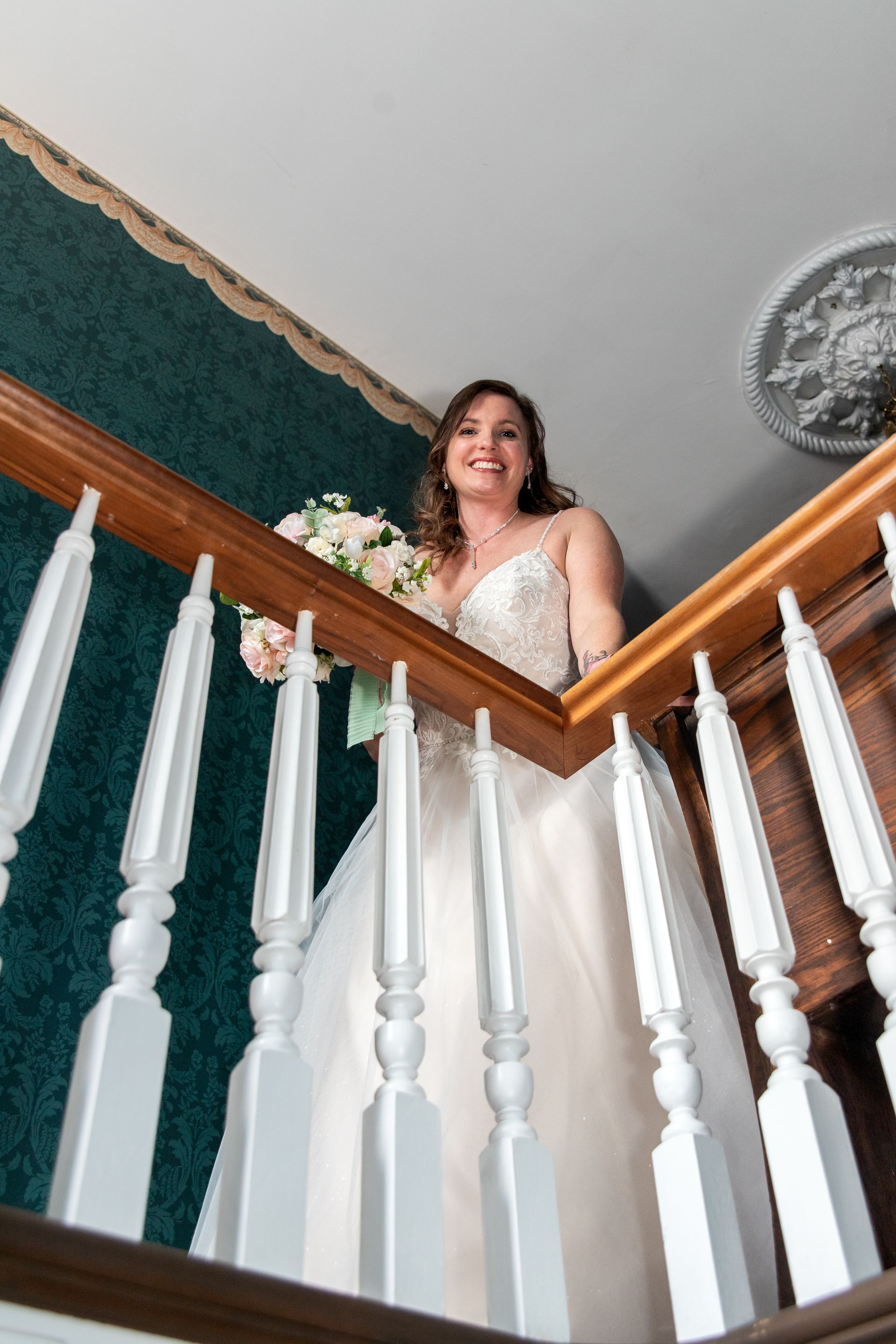 A bride in a wedding dress is standing on a staircase holding a bouquet of flowers.