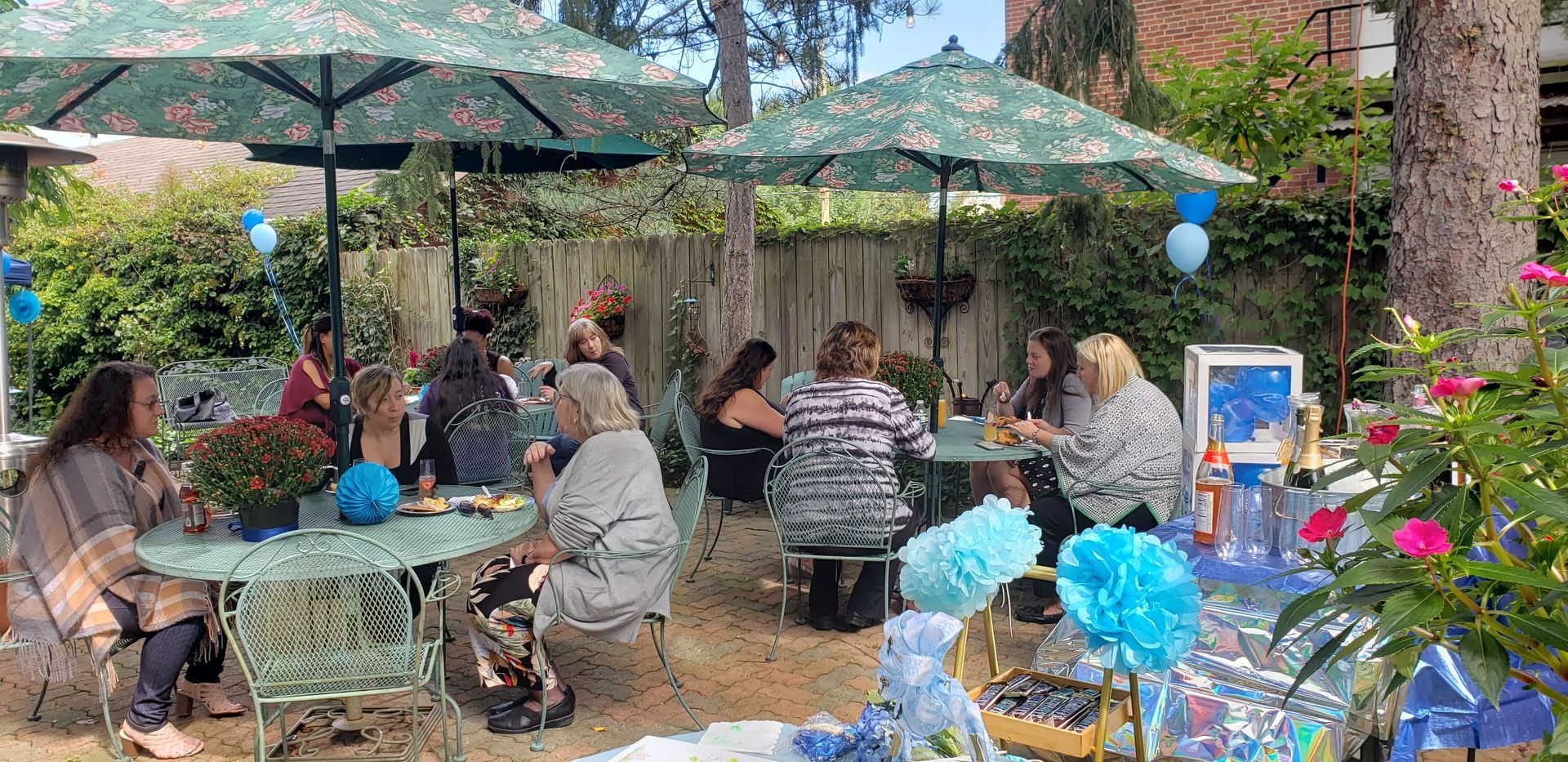 A group of people are sitting at tables under umbrellas in a garden.