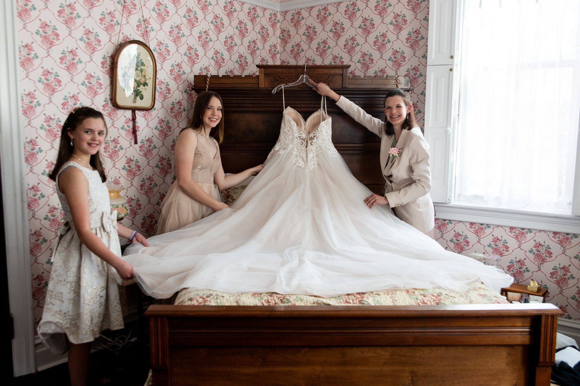 Three women are holding a bride 's wedding dress on a bed.