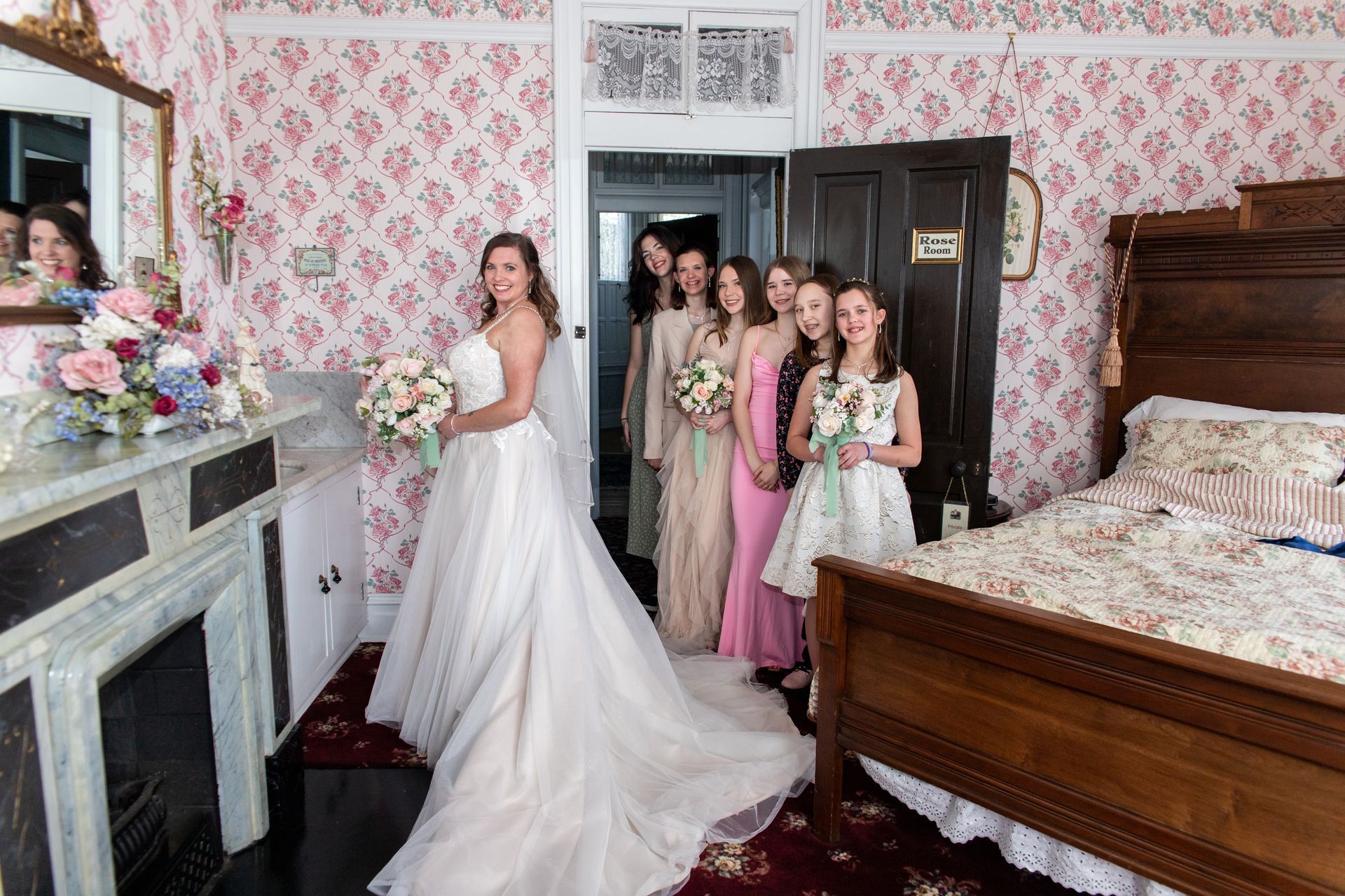 A bride and her bridesmaids are posing for a picture in a bedroom.