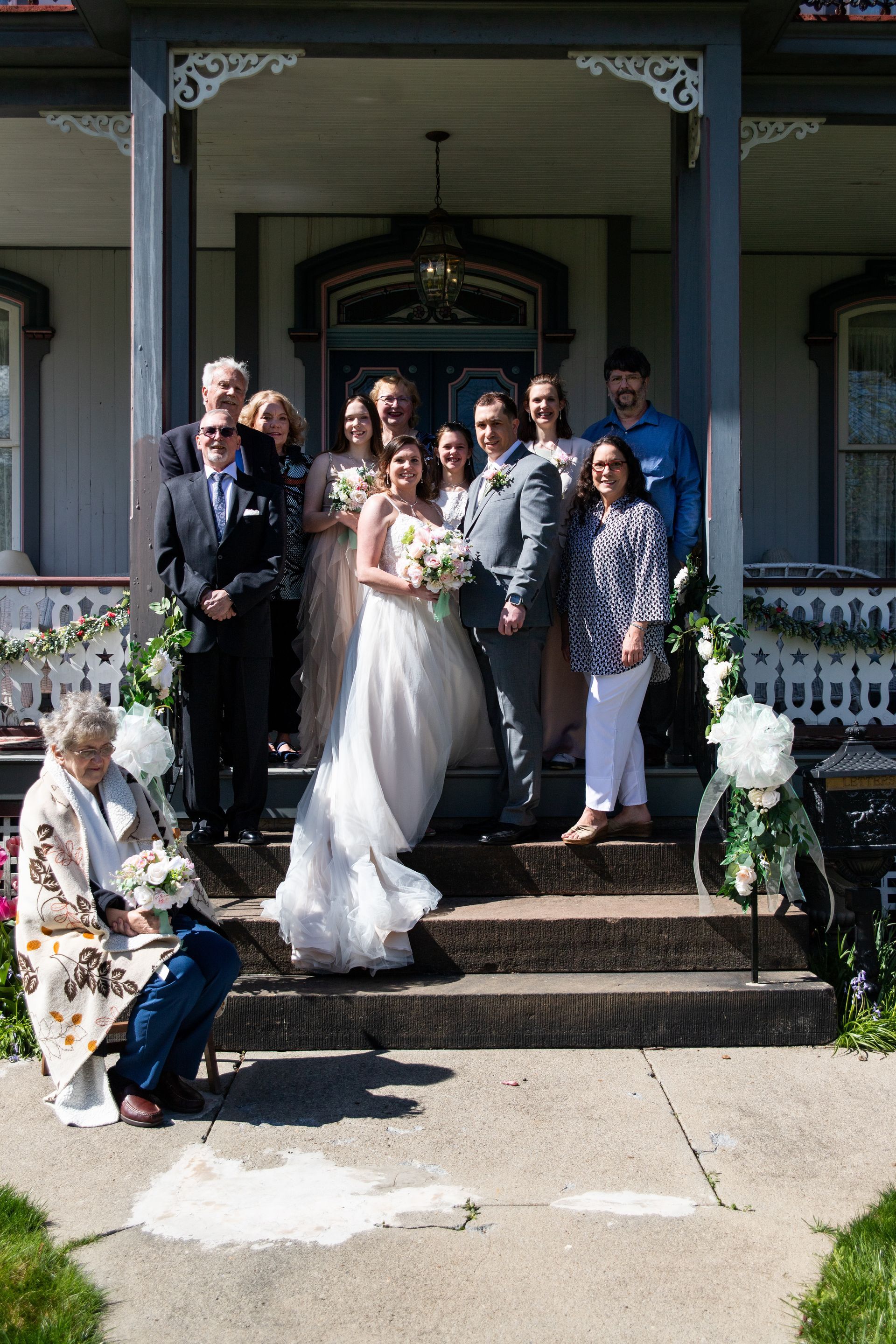 A bride and groom are posing for a picture with their family on the steps of a house.