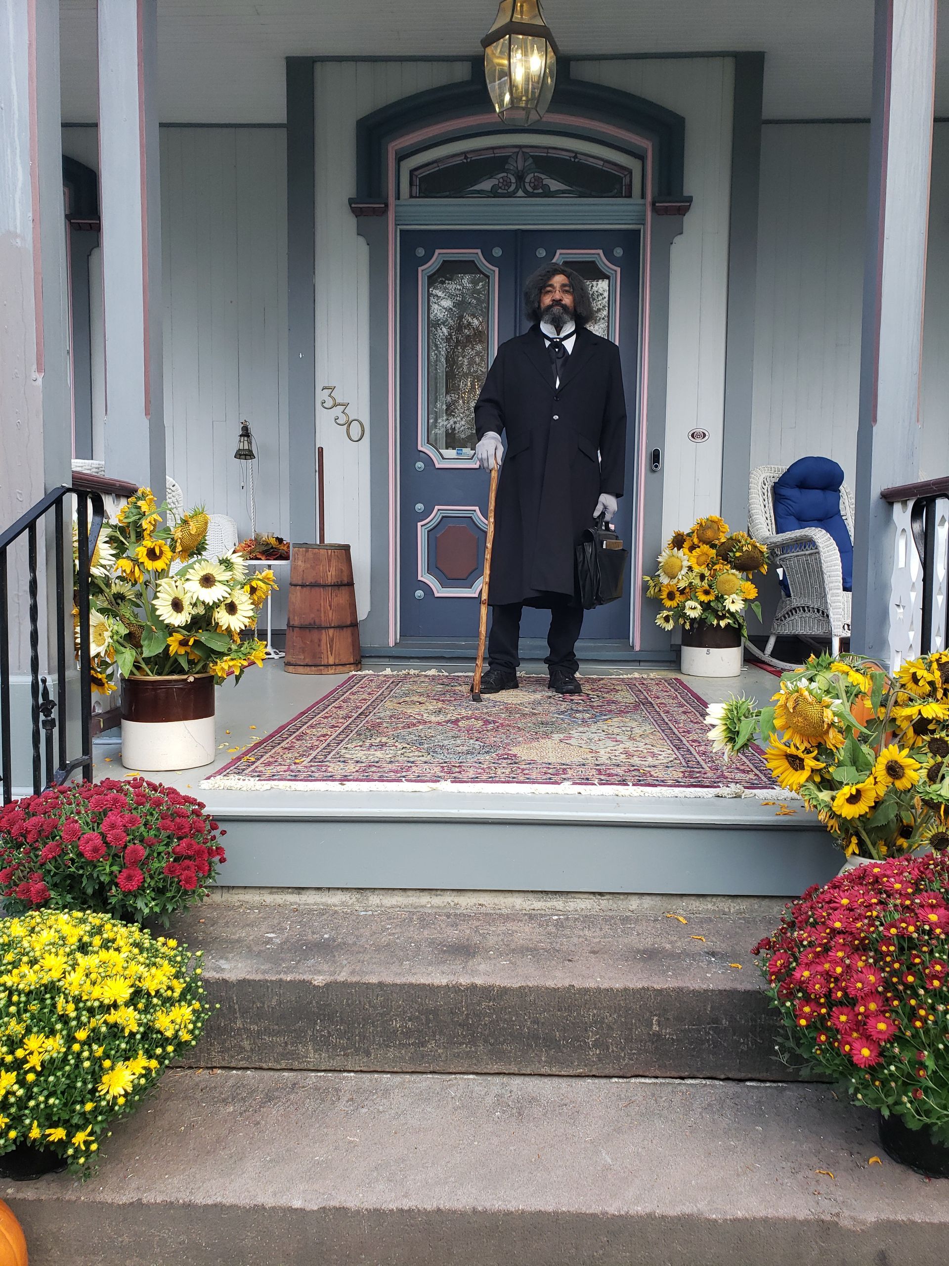 A man standing on a porch with flowers and pumpkins