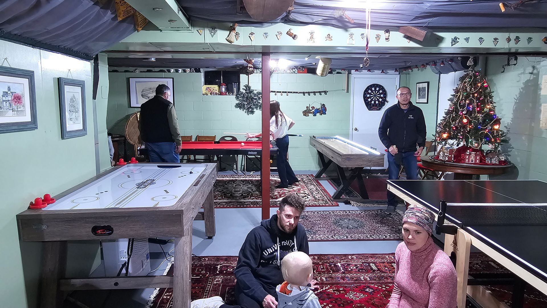 A group of people are playing pool and ping pong in a basement