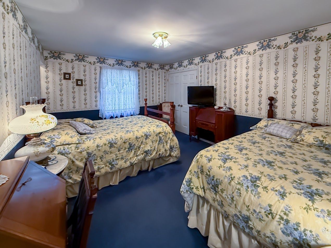 Bedroom with two double beds, floral wallpaper, blue carpet, and dark wood furniture.