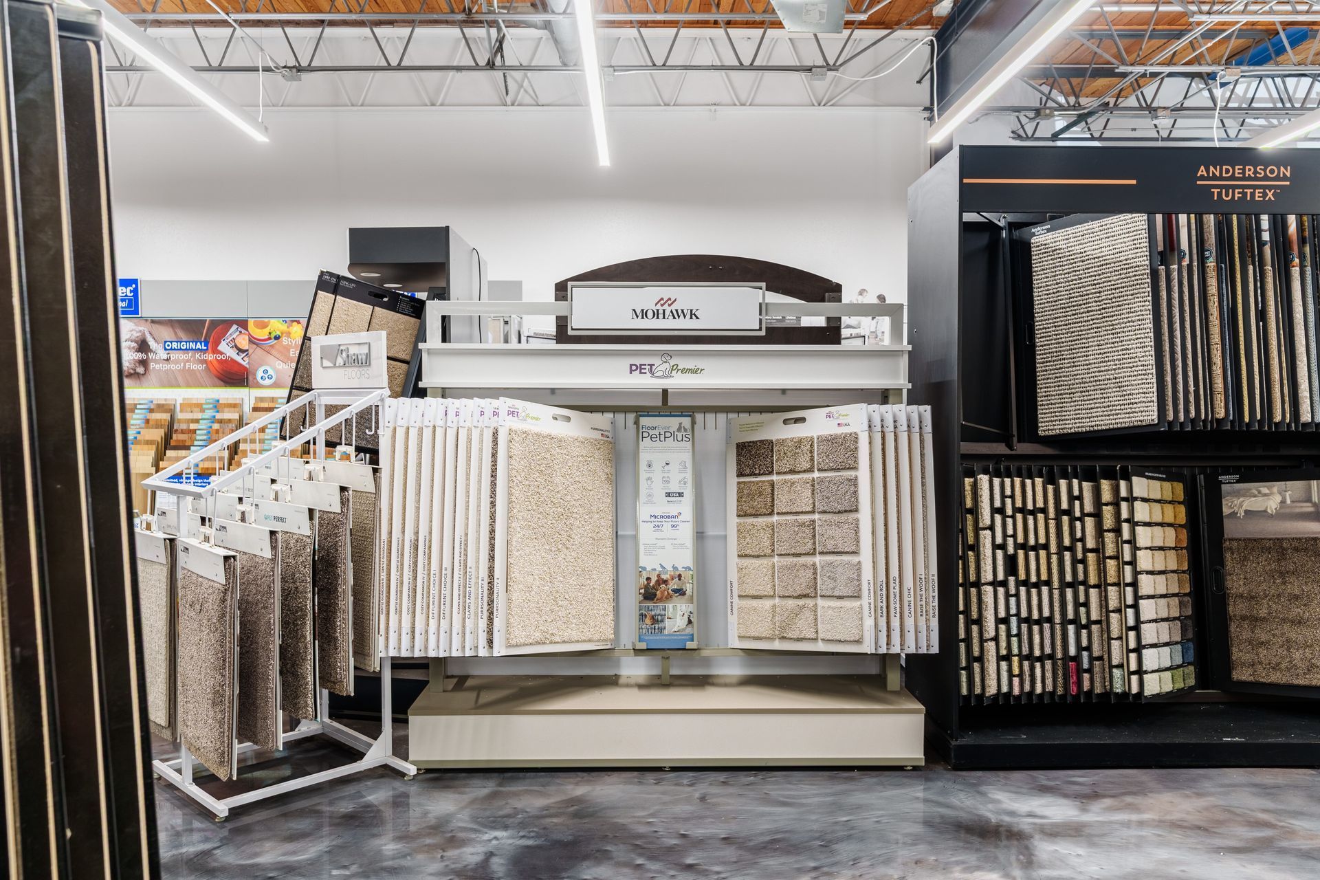 Carpet display aisle in a store, with hanging samples and shelving on both sides.