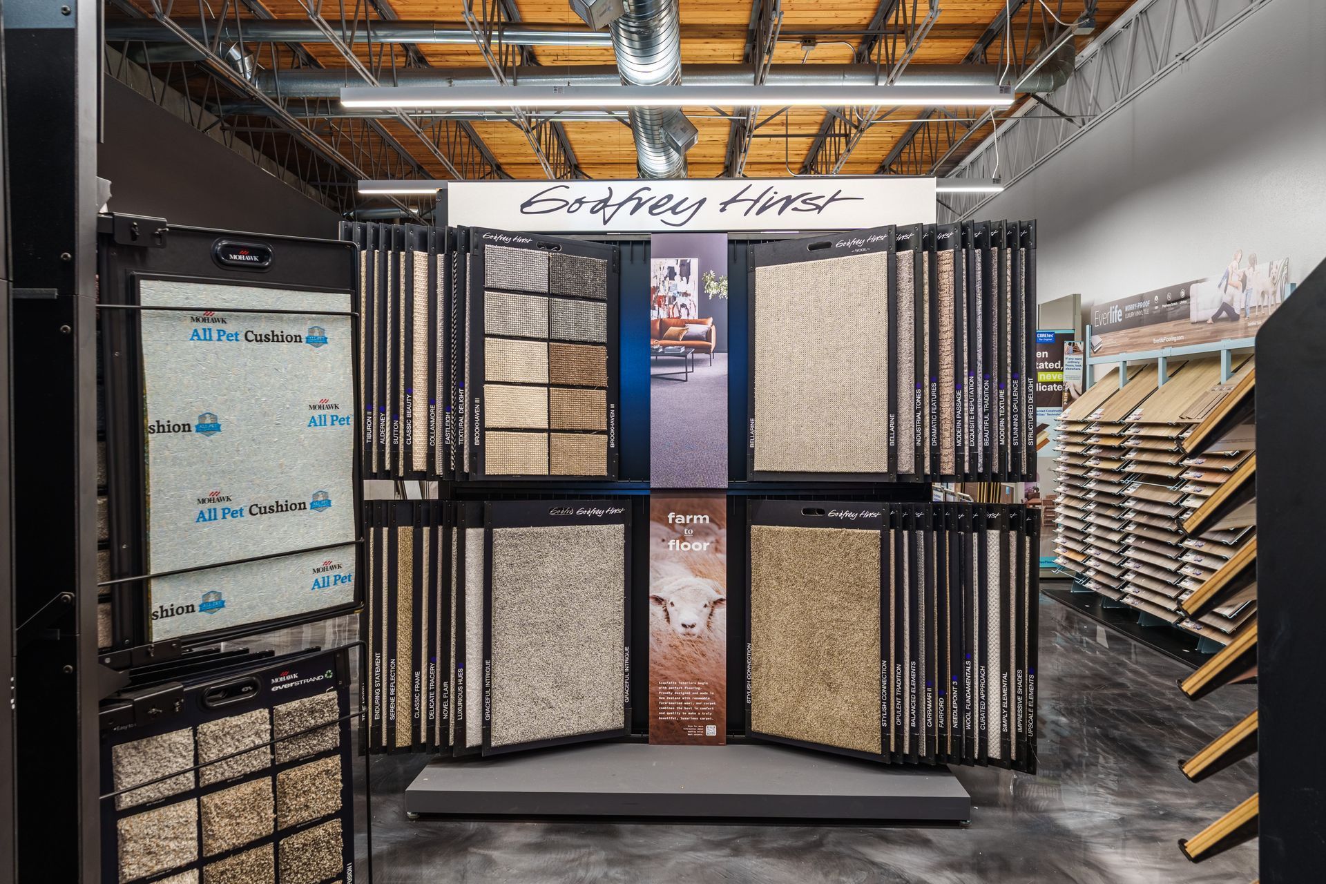 Carpet display in a warehouse aisle with hanging carpet samples and stacked rugs on shelves