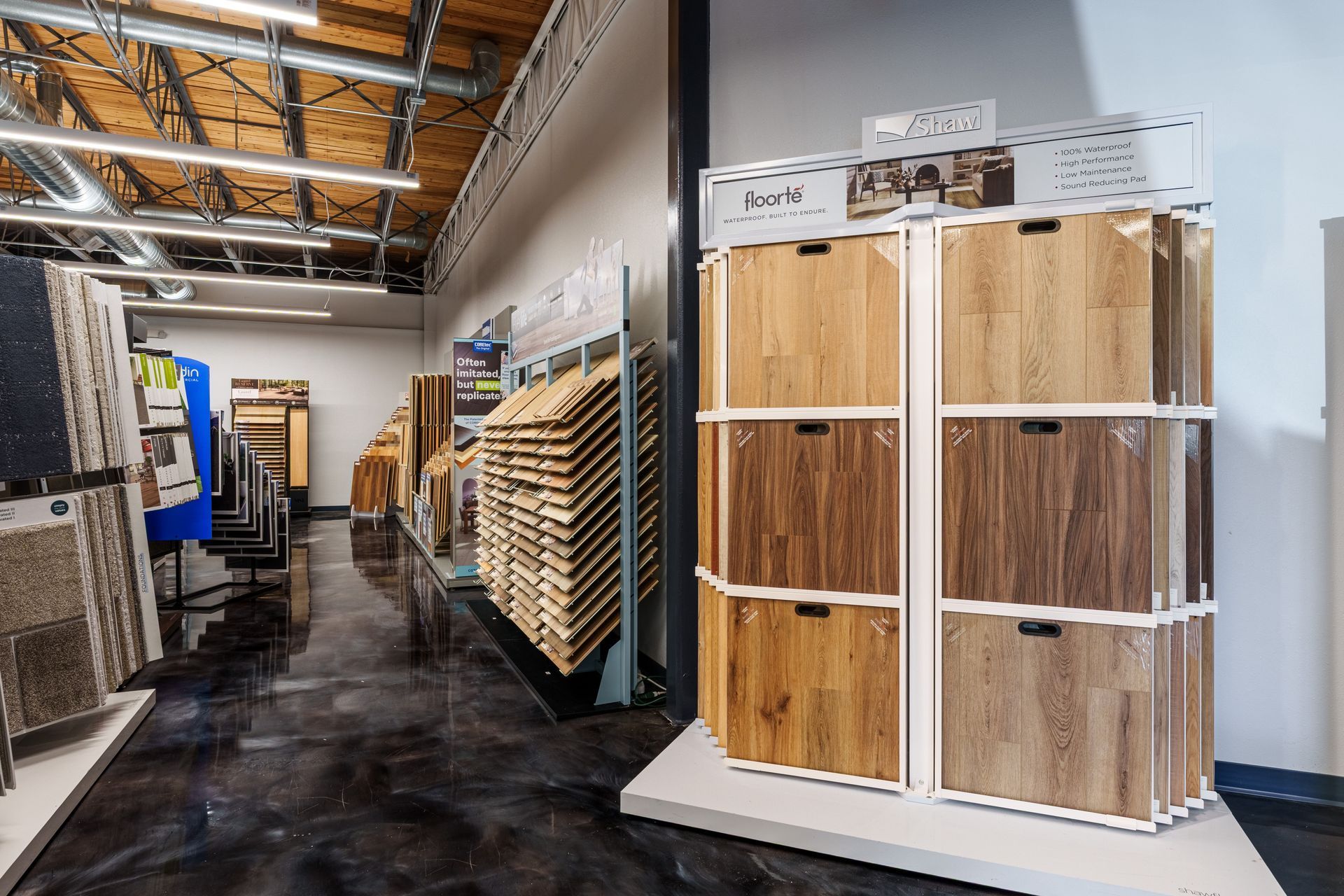 A store aisle with wood flooring samples displayed on racks and a high industrial ceiling.