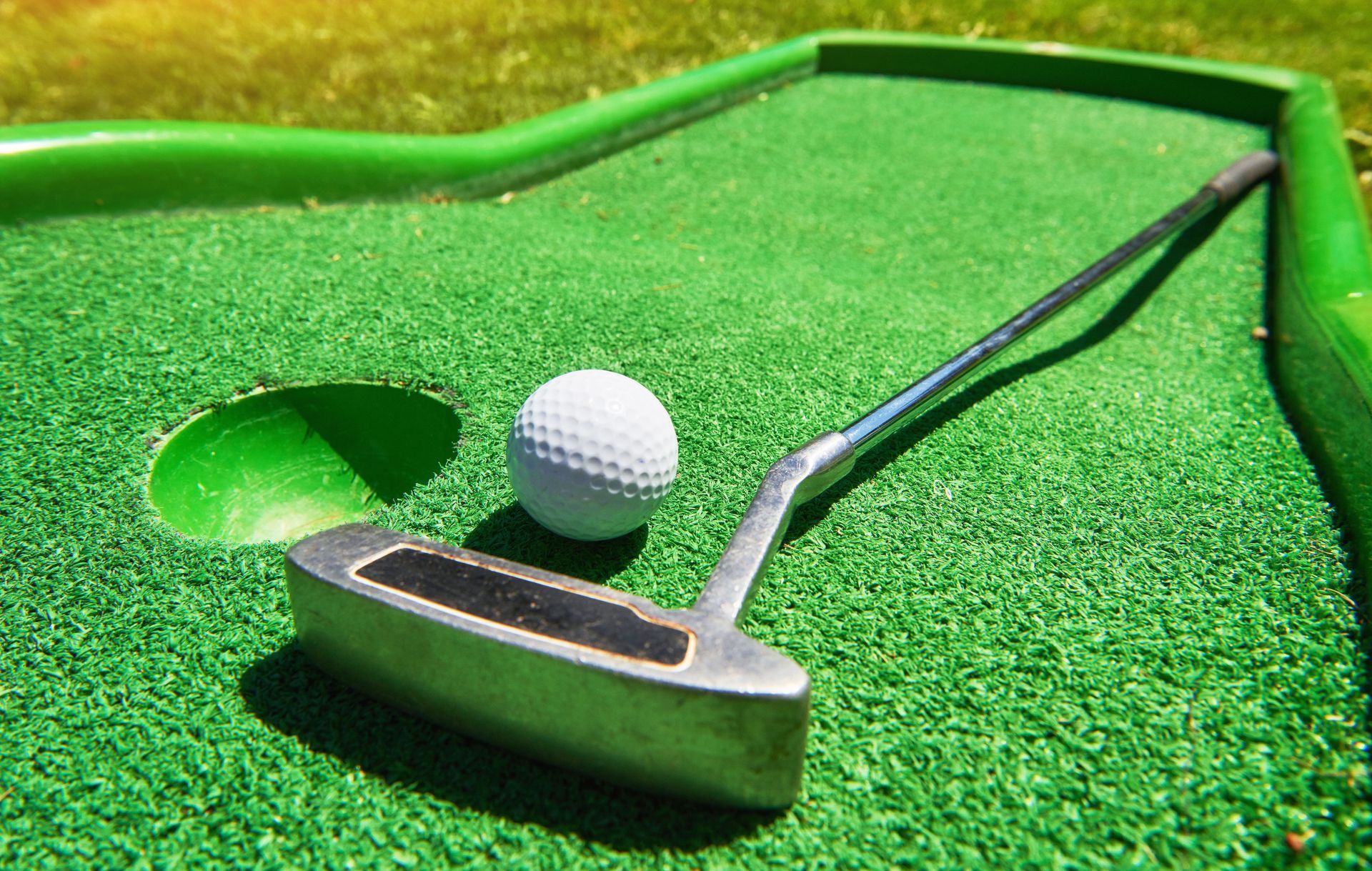 Miniature golf scene: white golf ball near hole and putter on green turf.