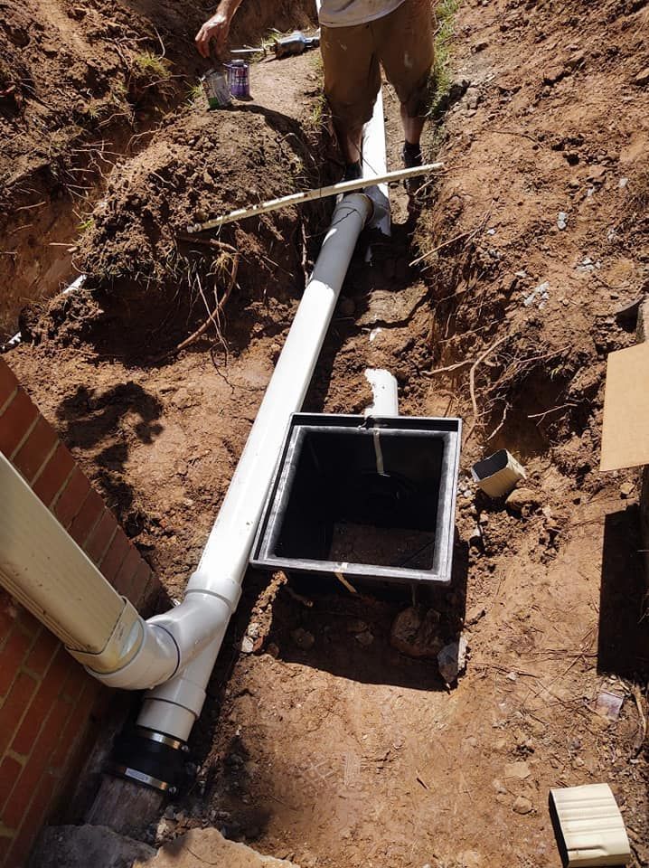 A man is working on a drain pipe in the dirt.