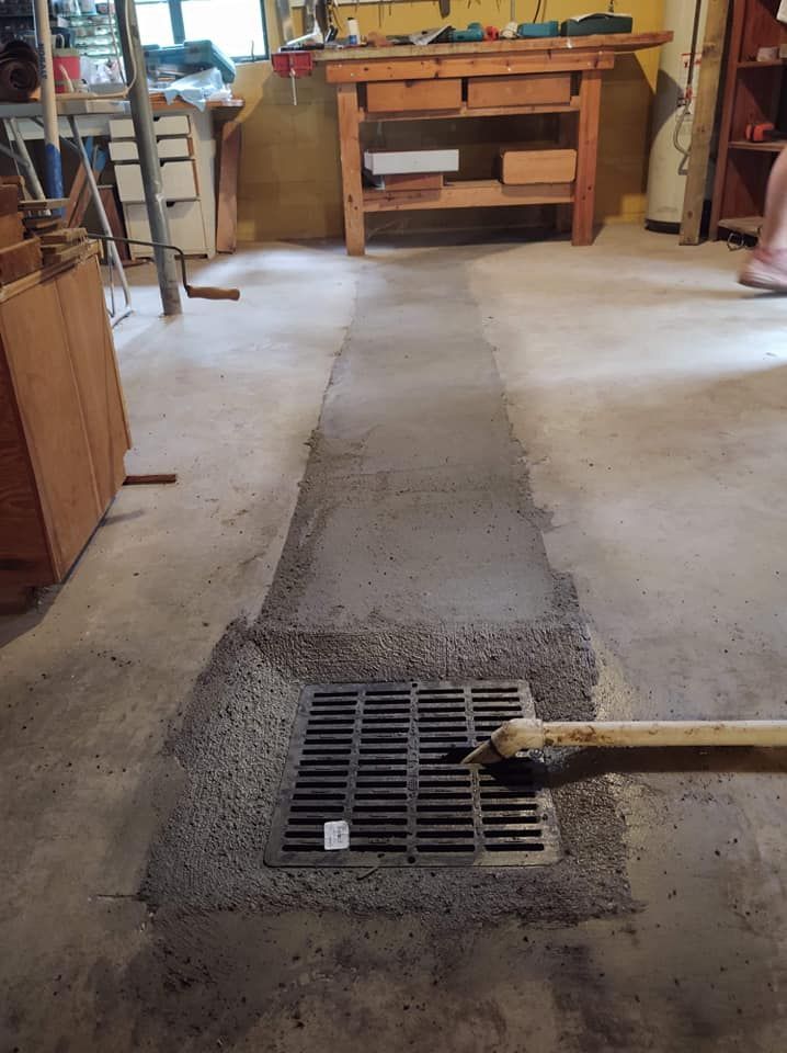 A drain in the floor of a garage with a wooden workbench in the background