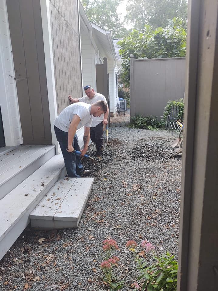 Two men are working on a sidewalk in front of a house.