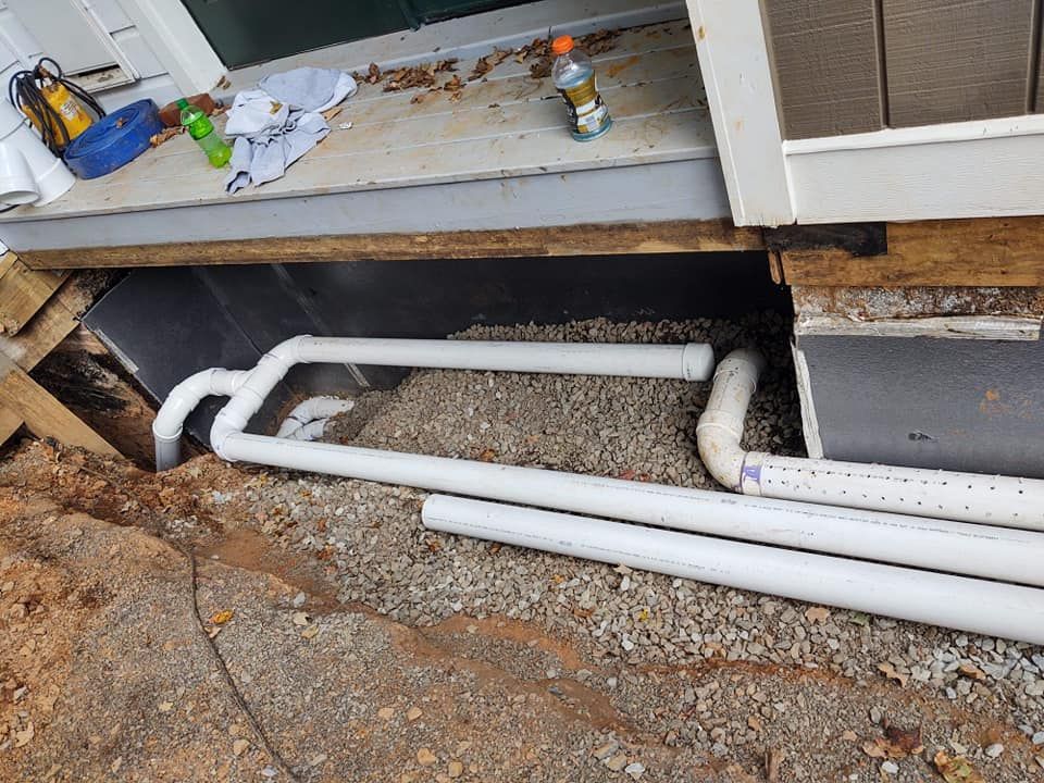 A bunch of pipes are laying on the ground next to a house.