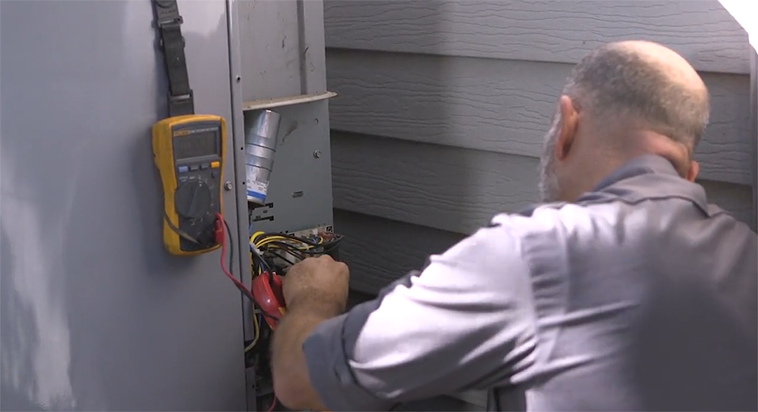 A man is working on an air conditioner with a multimeter.