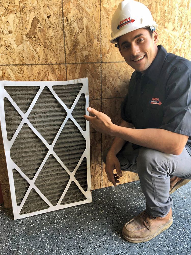 A man wearing a hard hat is kneeling down next to a dirty air filter.