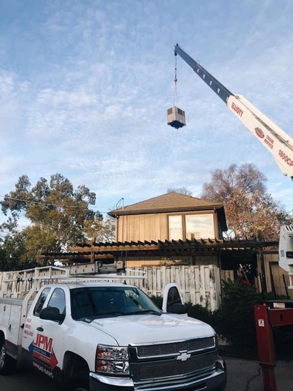 A white truck is parked in front of a house with a crane lifting a box.