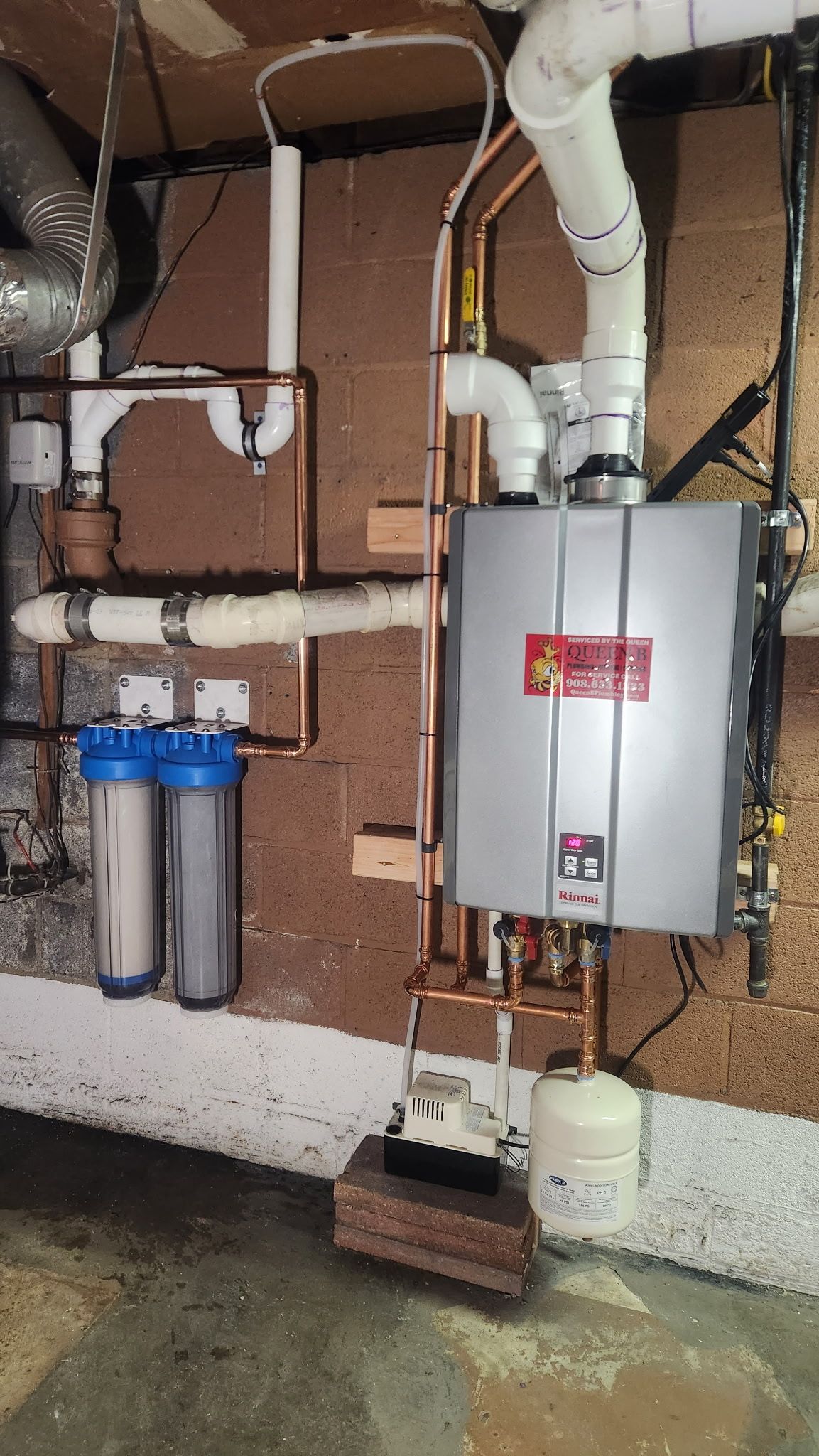 Basement utility room with furnace, white ductwork, water filter, and exposed pipes against brick wall