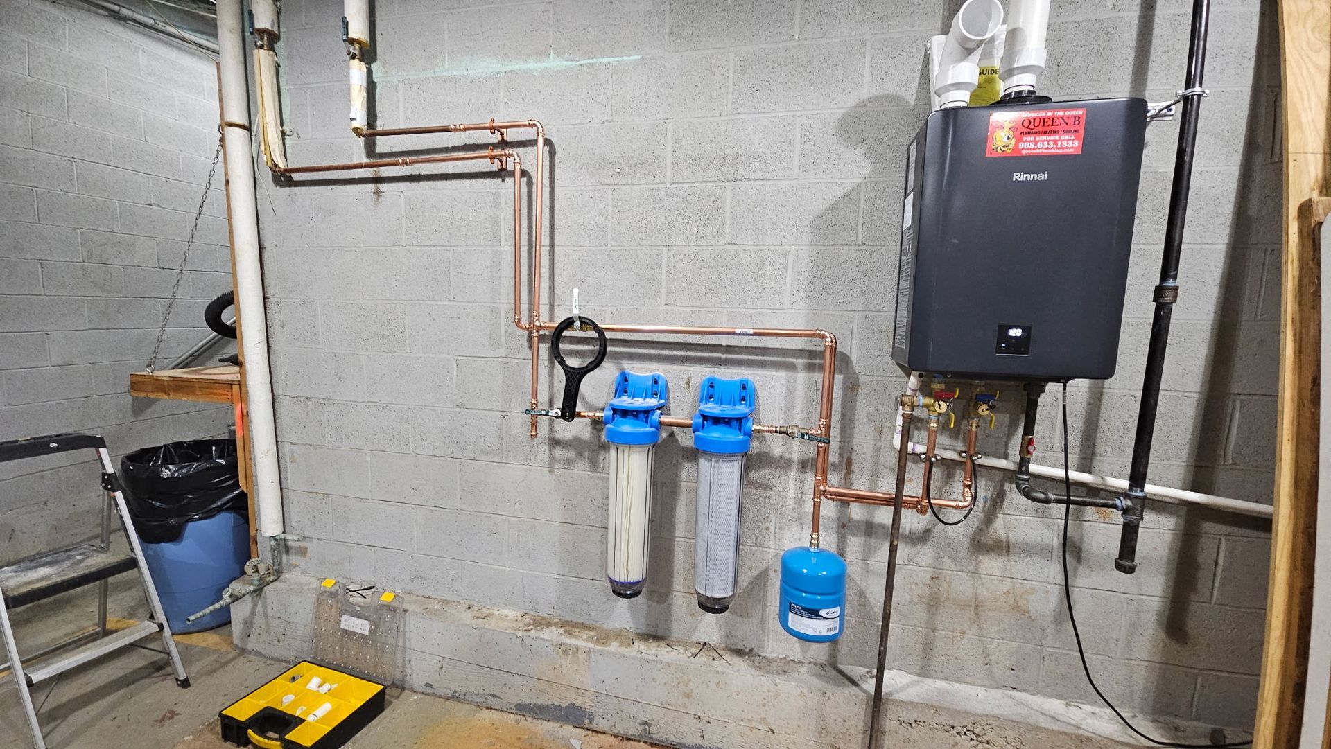 Basement wall with copper pipes, water filters, and a black tankless water heater.