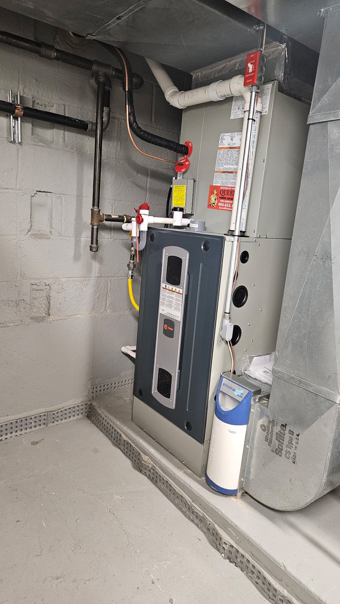 Gray industrial furnace and HVAC equipment in a utility room with pipes and a blue canister.