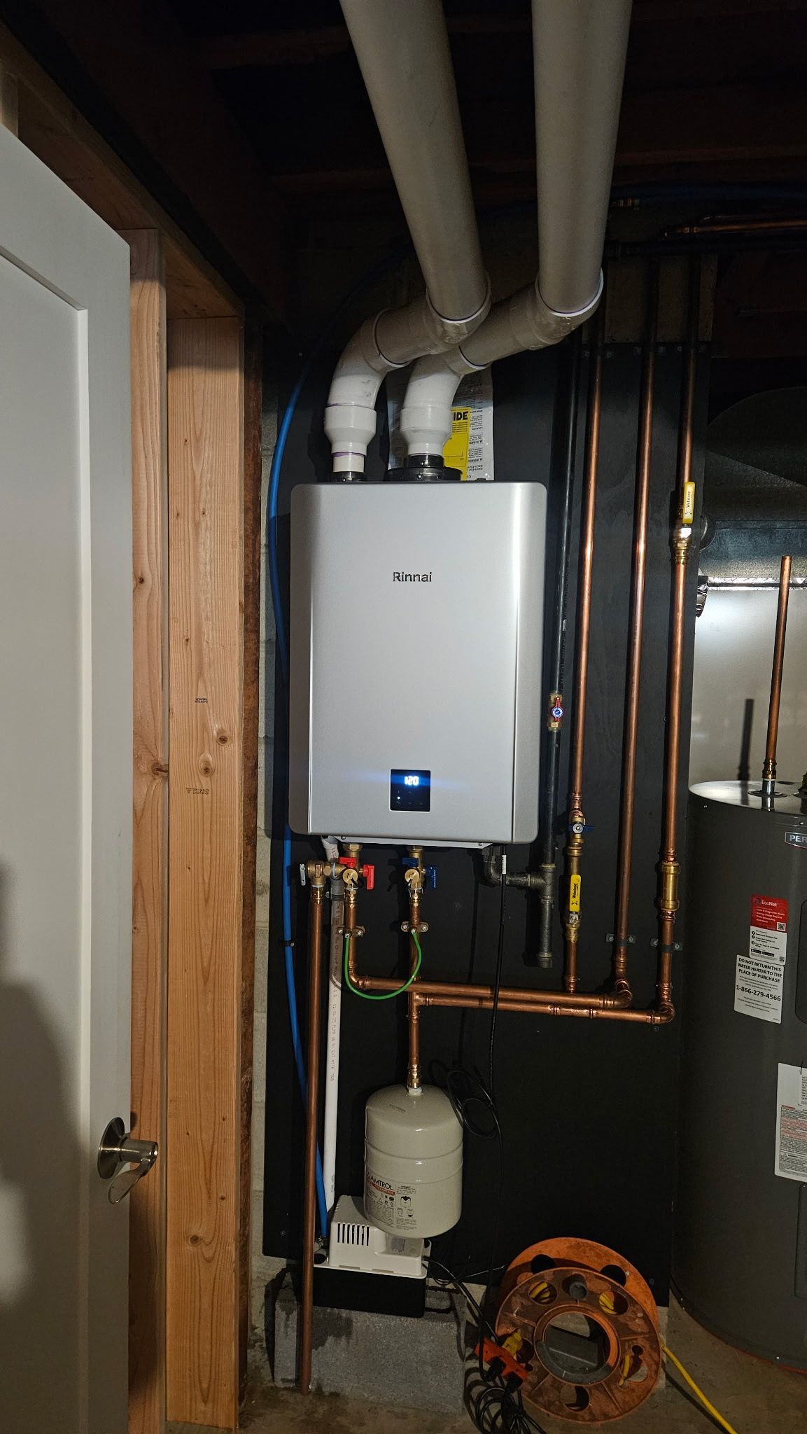 Utility room with white wall-mounted boiler, exposed pipes, and furnace equipment.