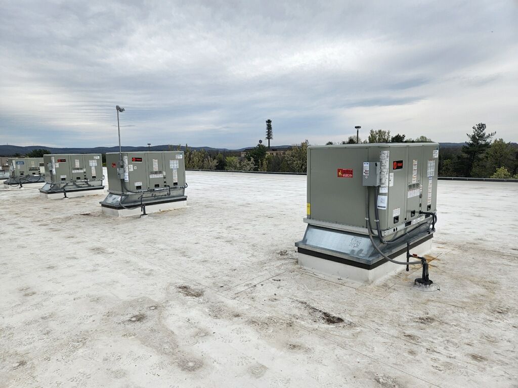 Row of gray utility generators on a snowy rooftop under an overcast sky
