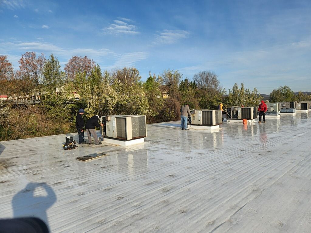 Rooftop with workers and HVAC units under a clear blue sky, wet reflective surface after rain