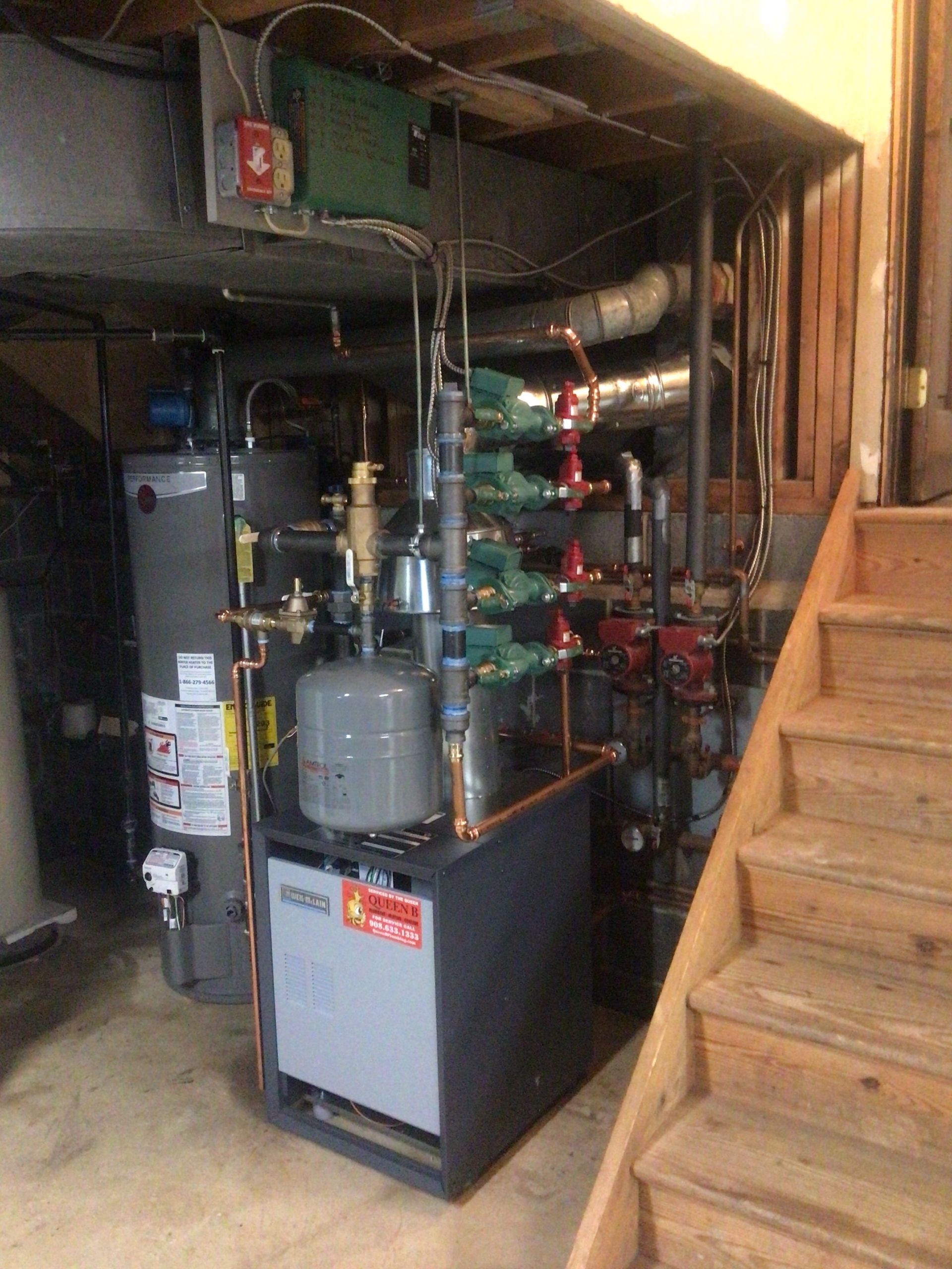 Basement utility room with boiler, pipes, and water heater beside wooden stairs