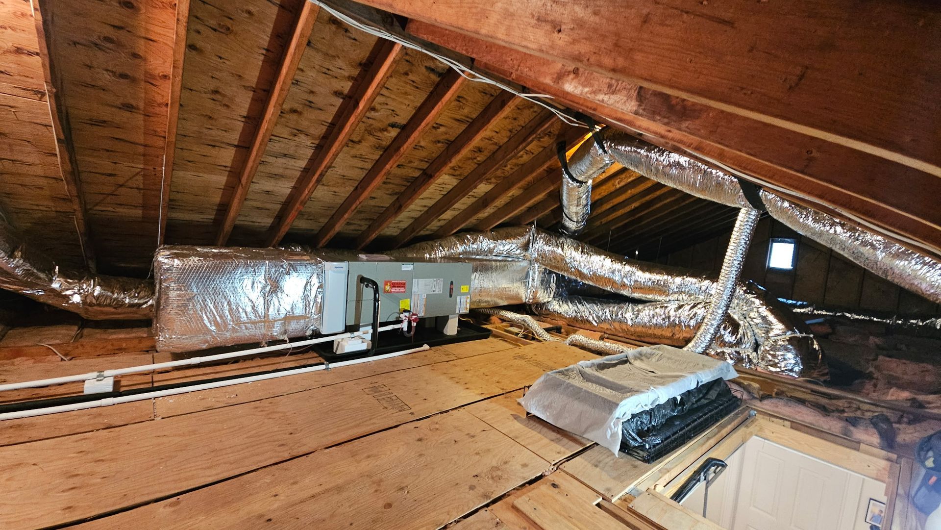 Attic with HVAC ducts, insulation, and exposed wooden rafters.
