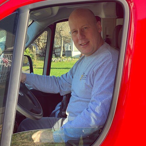 Man sitting in the driver’s seat of a red truck, looking at the camera.
