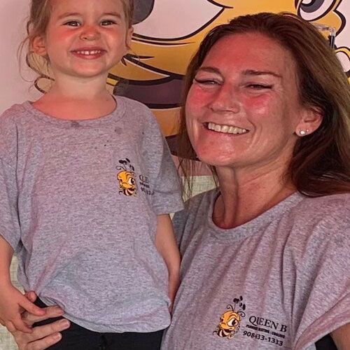 Woman and smiling child in gray shirts posing indoors in front of a cartoon mural