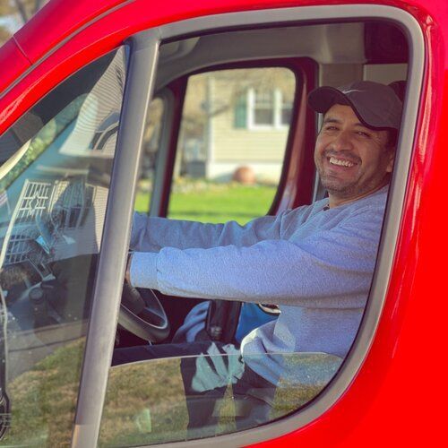 Smiling driver in a red truck, seen through the window, with hands on the steering wheel.