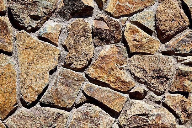 Close-up of a wall constructed of irregular, tan and brown stones with gray mortar.
