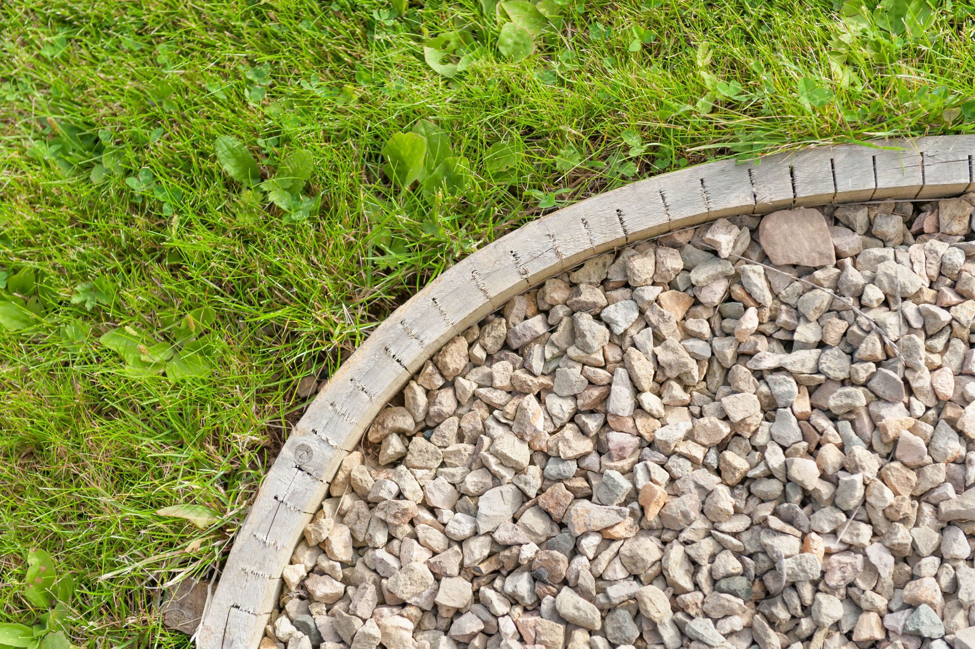 Green grass borders a gravel-filled area, defined by a curved concrete edge.