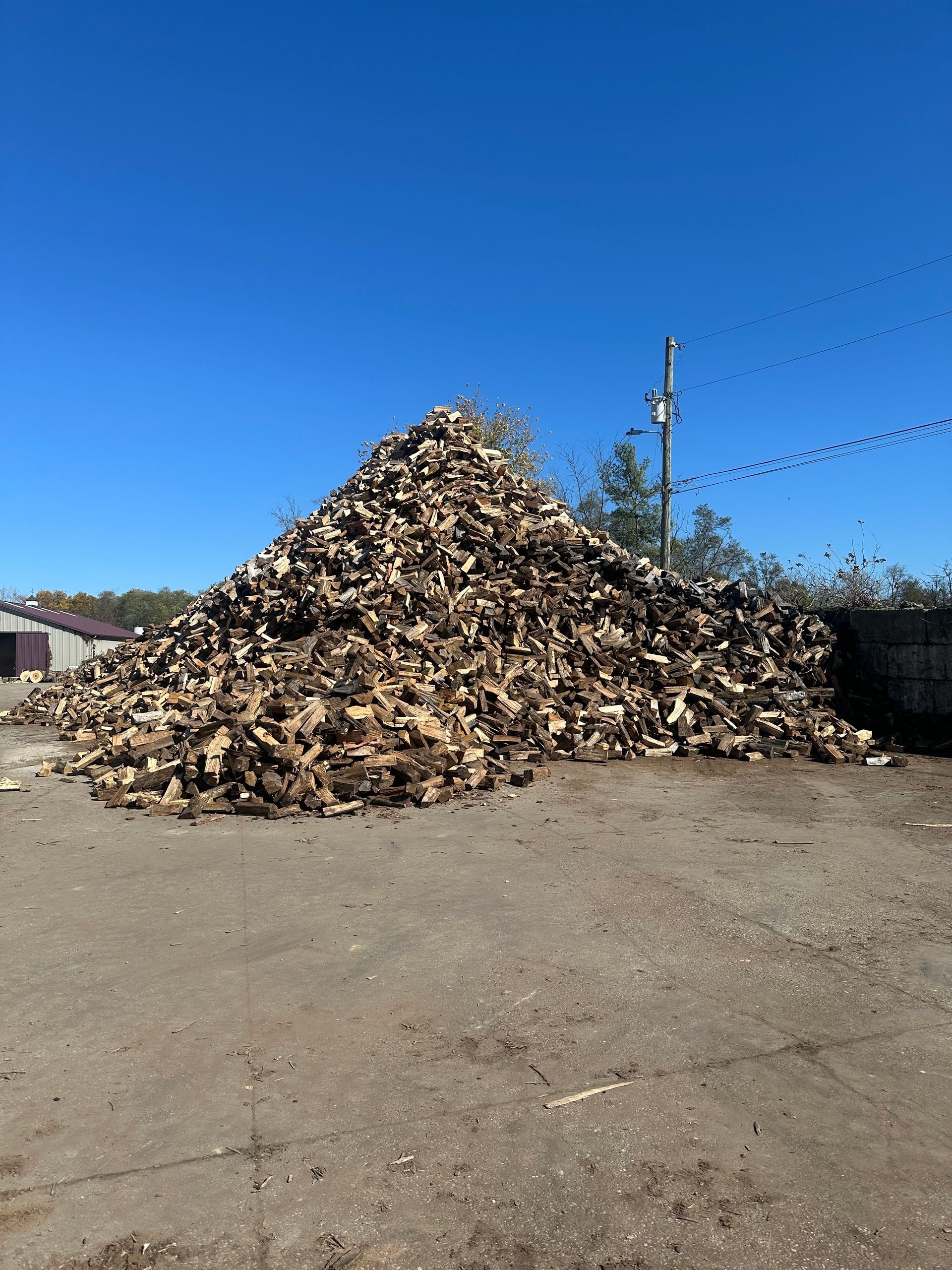 Large pile of firewood on a concrete surface against a clear blue sky.