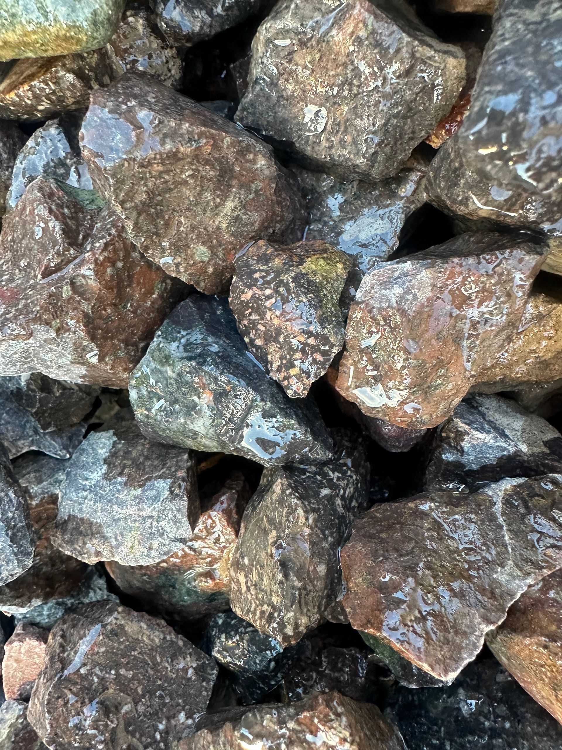 Pile of dark, wet rocks with brown, gray, and blue tones, possibly landscaping material.